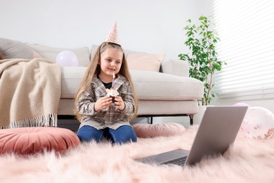 Photo of Birthday celebration. Little girl with cupcake having video call via laptop at home