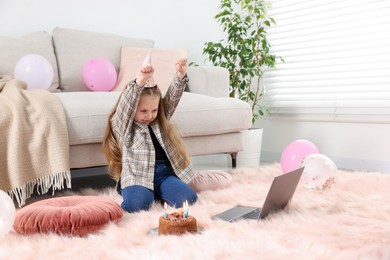 Photo of Birthday celebration. Little girl with cake having video call via laptop at home