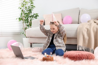 Photo of Birthday celebration. Little girl with cake having video call via laptop at home