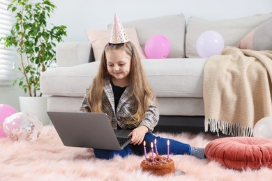 Photo of Birthday celebration. Little girl with cake having video call via laptop at home