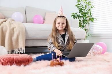 Photo of Birthday celebration. Little girl with cake having video call via laptop at home