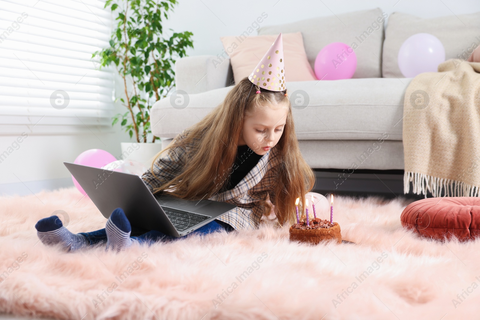 Birthday celebration. Little girl blowing candles on cake having video call via laptop at home Photo of Birthday celebration. Little girl blowing candles on cake having video call via laptop at home
