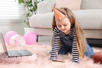 Photo of Birthday celebration. Little girl with piece of cake having video call via laptop at home