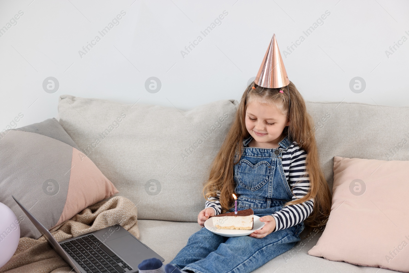 Birthday celebration. Little girl with piece of cake having video call via laptop on sofa at home Photo of Birthday celebration. Little girl with piece of cake having video call via laptop on sofa at home