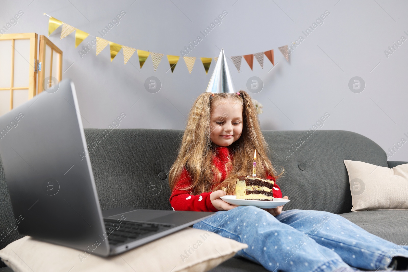 Birthday celebration. Little girl with piece of cake having video call via laptop on sofa at home Photo of Birthday celebration. Little girl with piece of cake having video call via laptop on sofa at home