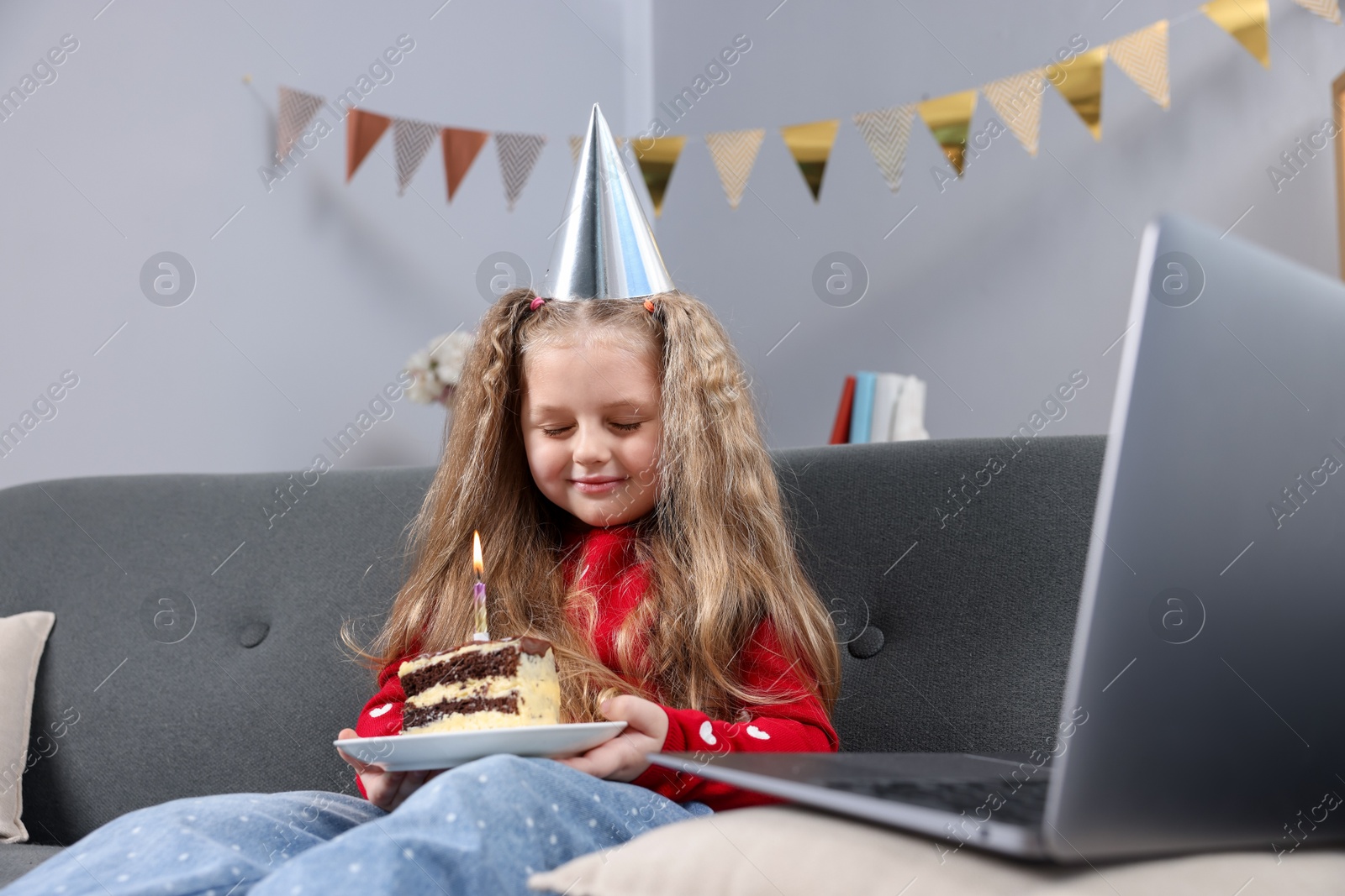 Birthday celebration. Little girl with piece of cake having video call via laptop on sofa at home Photo of Birthday celebration. Little girl with piece of cake having video call via laptop on sofa at home