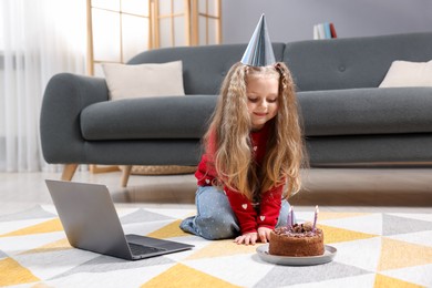 Photo of Birthday celebration. Little girl with cake having video call via laptop at home