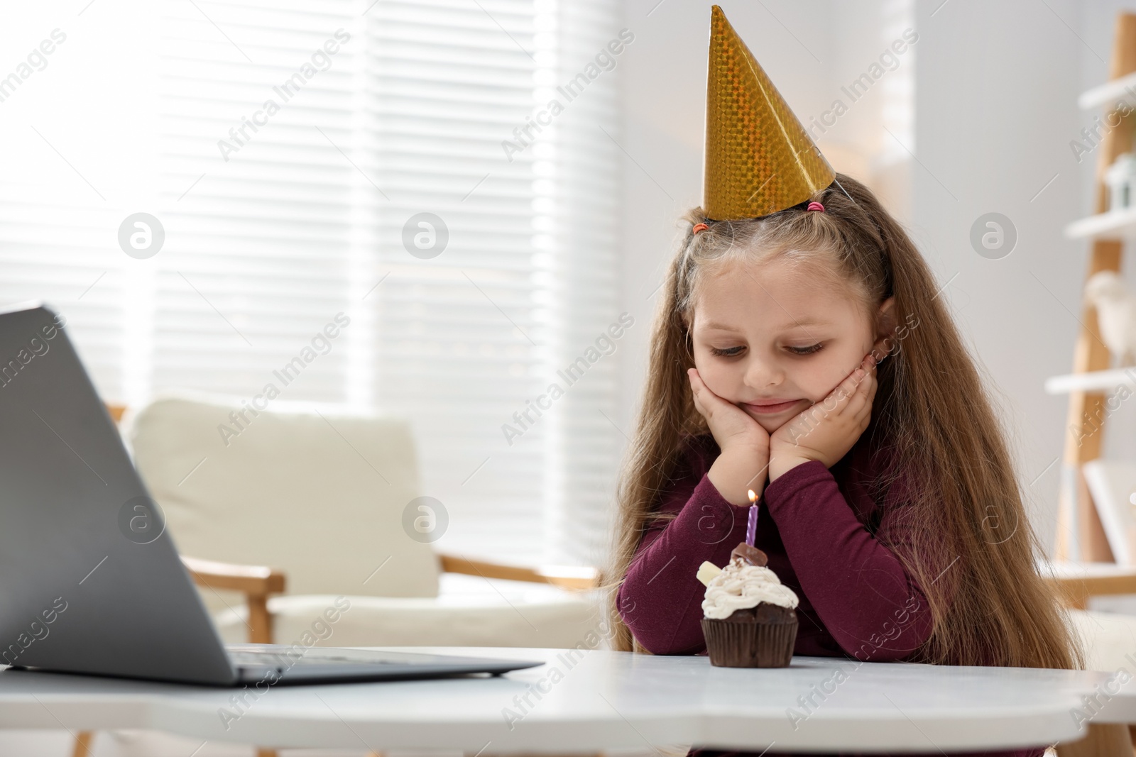 Birthday celebration. Little girl with cupcake having video call via laptop at table indoors Photo of Birthday celebration. Little girl with cupcake having video call via laptop at table indoors