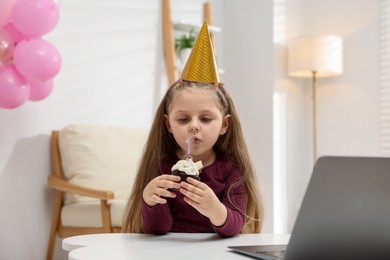 Photo of Birthday celebration. Little girl with cupcake having video call via laptop at table indoors