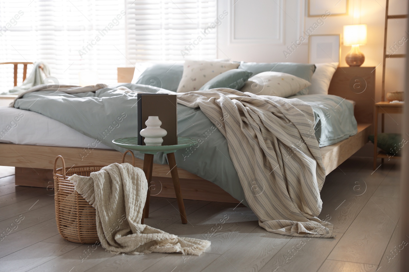 Comfortable bed with soft linens, lamp and decor in stylish room. Home textile Photo of Comfortable bed with soft linens, lamp and decor in stylish room. Home textile