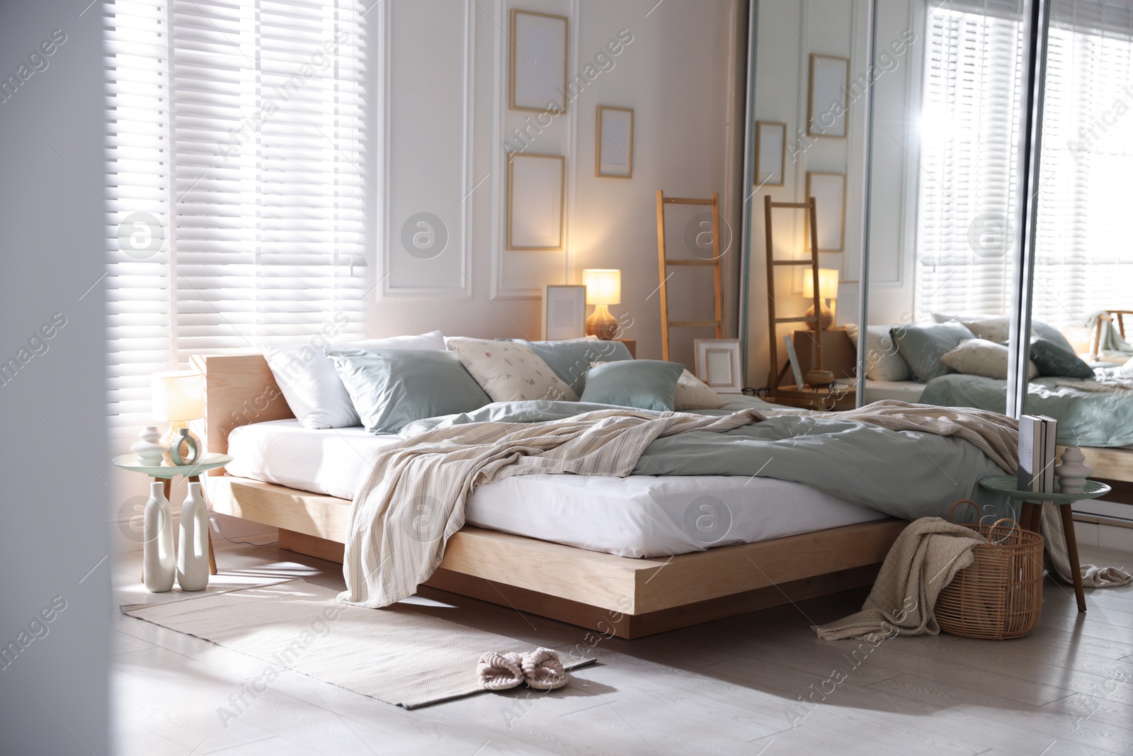 Comfortable bed with soft linens, lamp and decor in stylish room. Home textile Photo of Comfortable bed with soft linens, lamp and decor in stylish room. Home textile
