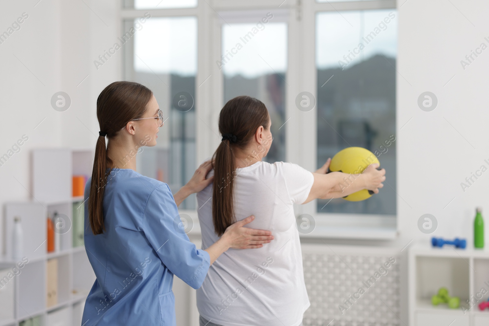 Doctor and patient exercising with medicine ball in clinic, back view Photo of Doctor and patient exercising with medicine ball in clinic, back view