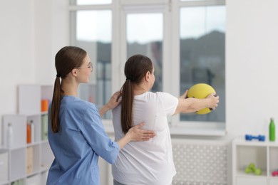 Photo of Doctor and patient exercising with medicine ball in clinic, back view