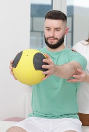 Photo of Doctor and patient exercising with medicine ball in clinic