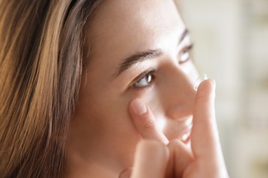 Photo of Beautiful woman putting in contact lens indoors, closeup