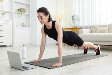 Photo of Woman doing plank exercise during online class with coach at home. Sport and healthy lifestyle