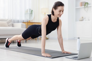 Photo of Woman doing plank exercise during online class with coach at home. Sport and healthy lifestyle