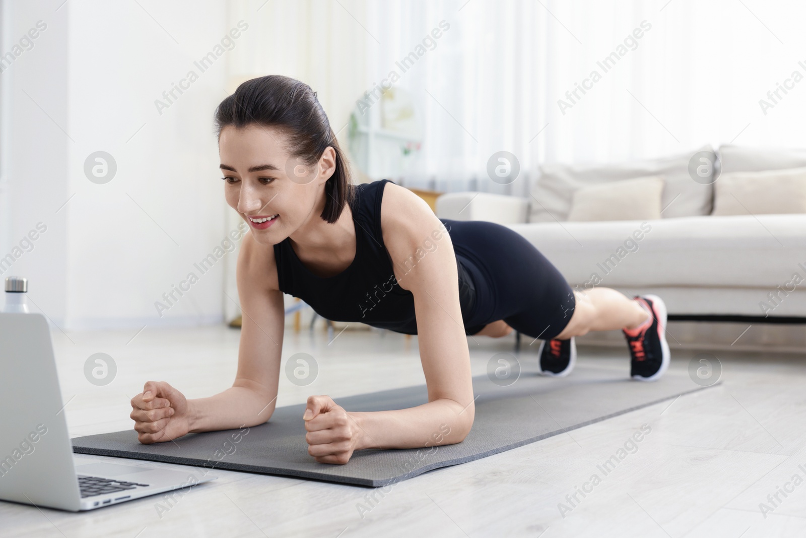 Woman doing plank exercise during online class with coach at home. Sport and healthy lifestyle Photo of Woman doing plank exercise during online class with coach at home. Sport and healthy lifestyle