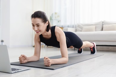 Photo of Woman doing plank exercise during online class with coach at home. Sport and healthy lifestyle