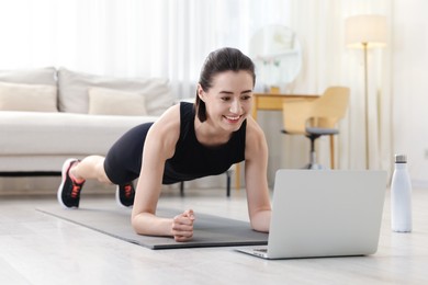 Photo of Woman doing plank exercise during online class with coach at home. Sport and healthy lifestyle