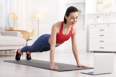 Photo of Woman doing plank exercise during online class with coach at home. Sport and healthy lifestyle