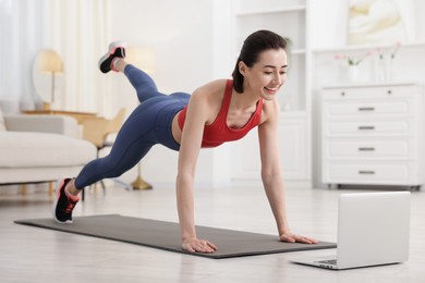 Photo of Woman doing plank exercise during online class with coach at home. Sport and healthy lifestyle