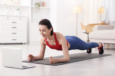 Photo of Woman doing plank exercise during online class with coach at home. Sport and healthy lifestyle