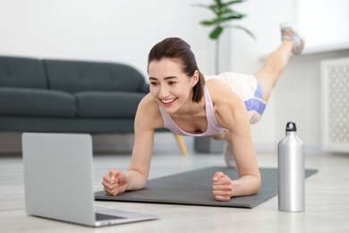 Photo of Woman doing plank exercise during online class with coach at home. Sport and healthy lifestyle