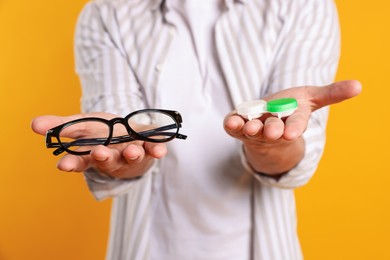 Photo of Man choosing between glasses and contact lenses on yellow background, closeup