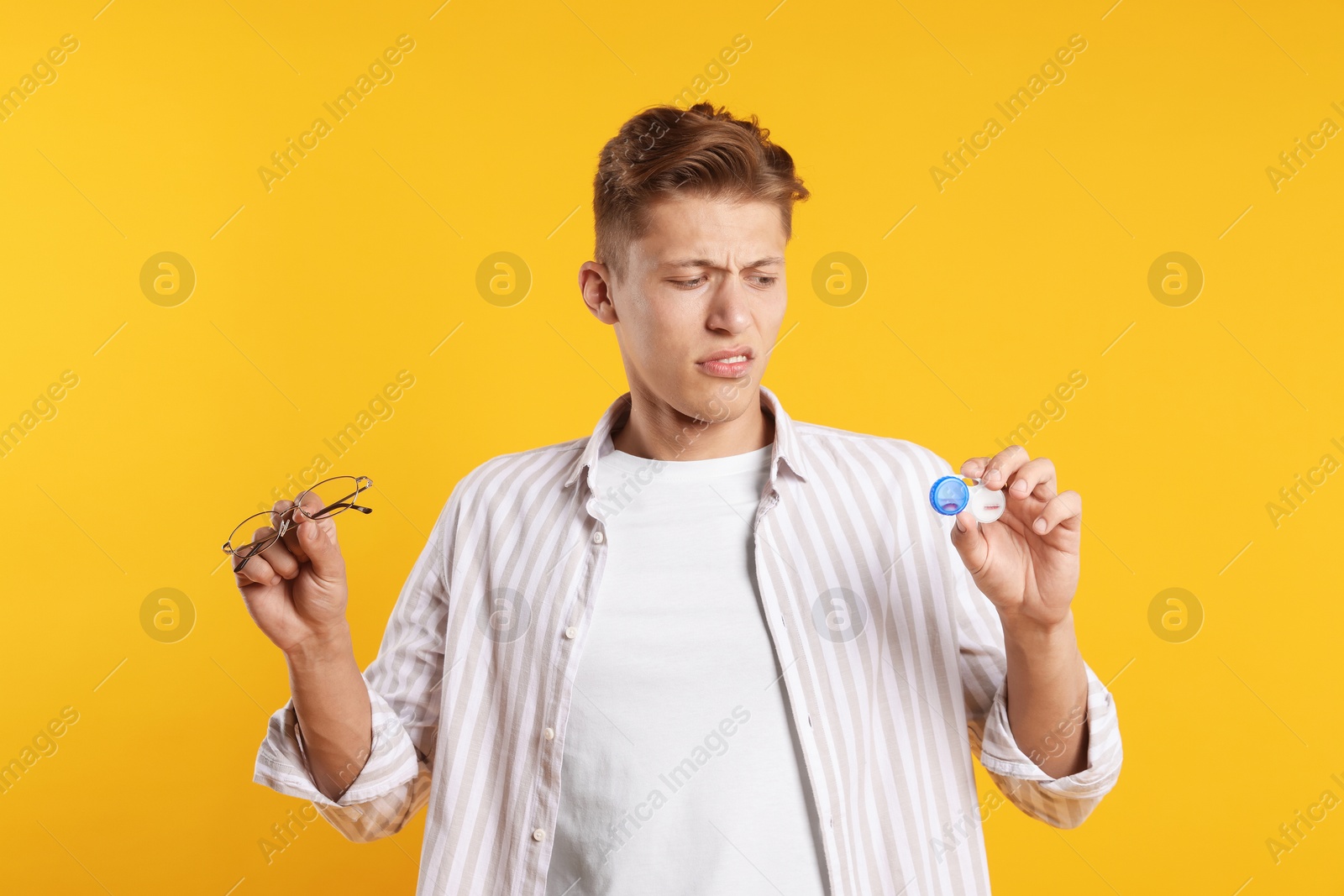Man choosing between glasses and contact lenses on yellow background Photo of Man choosing between glasses and contact lenses on yellow background