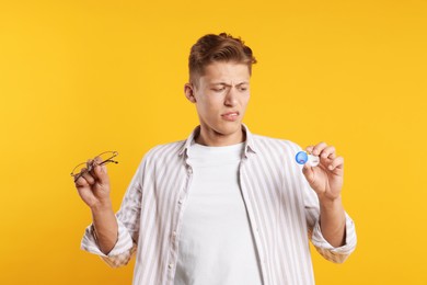 Photo of Man choosing between glasses and contact lenses on yellow background