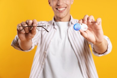 Photo of Man choosing between glasses and contact lenses on yellow background, closeup