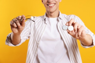 Photo of Man choosing between glasses and contact lenses on yellow background, closeup