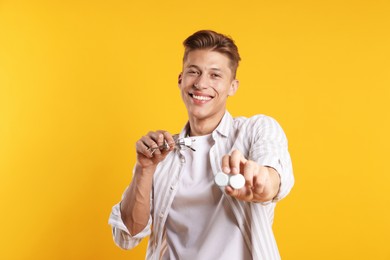 Photo of Man choosing between glasses and contact lenses on yellow background