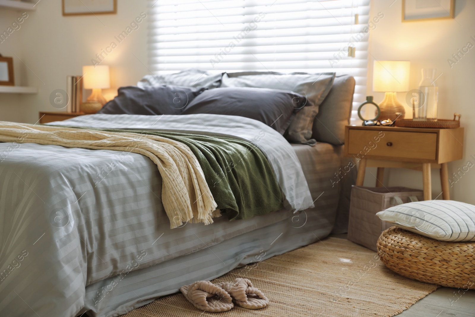 Comfortable bed with soft linens, blankets and slippers in room. Home textile Photo of Comfortable bed with soft linens, blankets and slippers in room. Home textile
