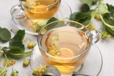 Photo of Fresh linden tea in cups and flowers on light grey table, closeup