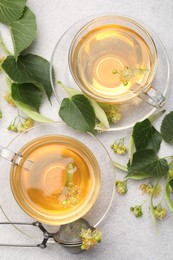 Photo of Fresh linden tea in cups and flowers on light grey table, flat lay
