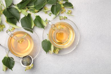 Photo of Fresh linden tea in cups and flowers on light grey table, flat lay. Space for text