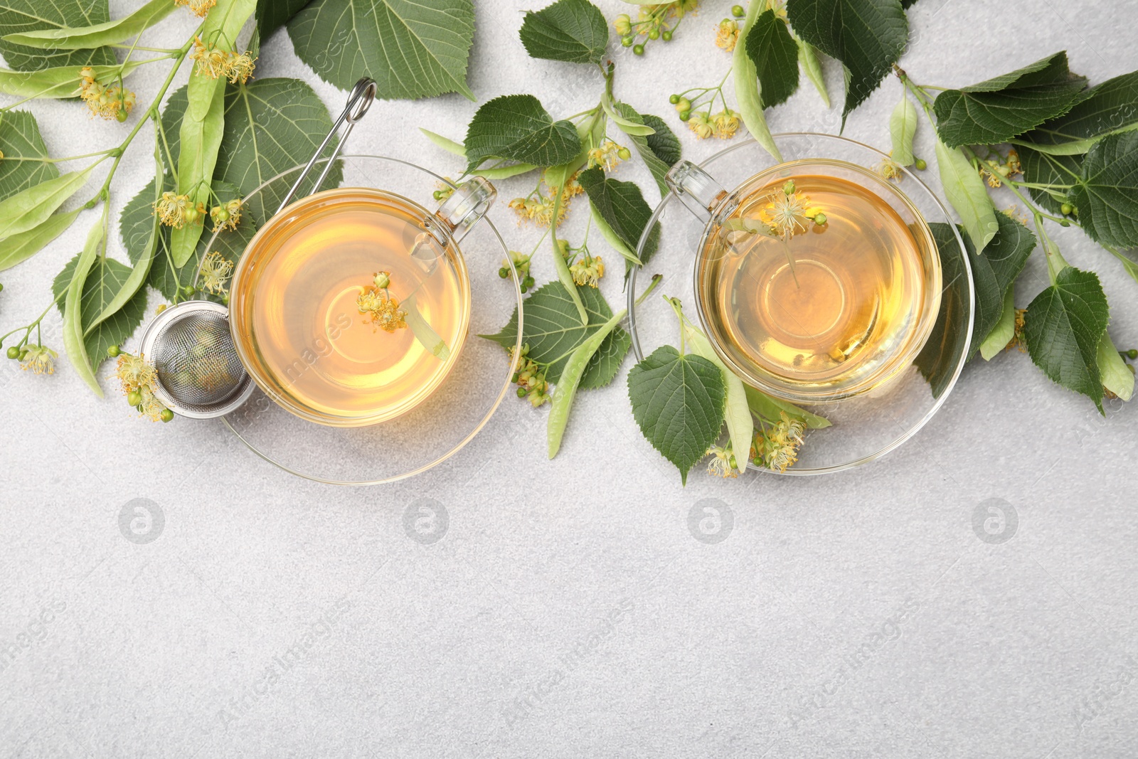 Fresh linden tea in cups and flowers on light grey table, flat lay. Space for text Photo of Fresh linden tea in cups and flowers on light grey table, flat lay. Space for text