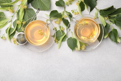 Photo of Fresh linden tea in cups and flowers on light grey table, flat lay. Space for text
