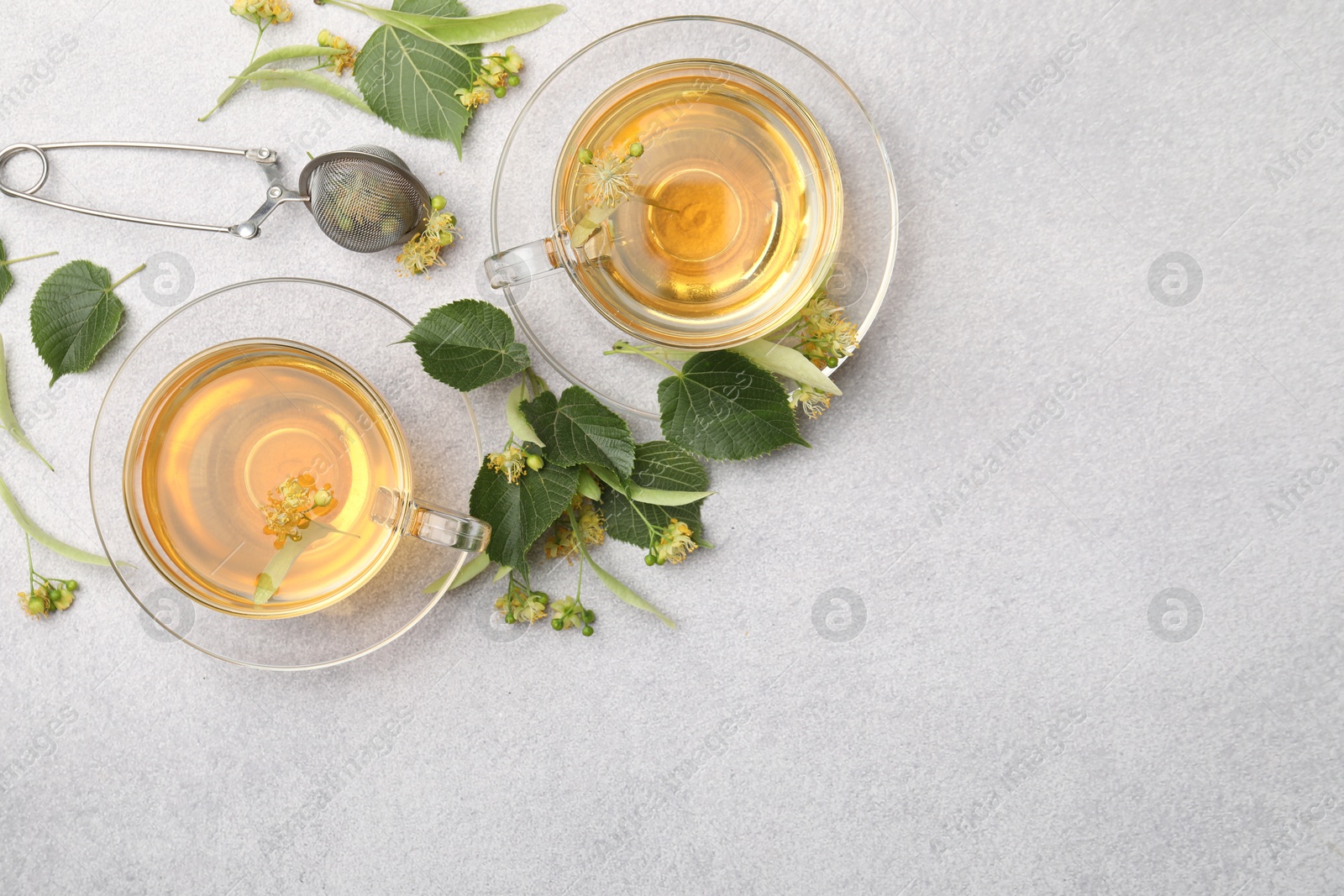 Fresh linden tea in cups and flowers on light grey table, flat lay. Space for text Photo of Fresh linden tea in cups and flowers on light grey table, flat lay. Space for text