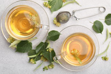 Photo of Fresh linden tea in cups and flowers on light grey table, flat lay