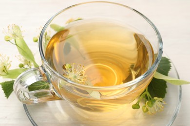 Photo of Fresh linden tea in cup and flowers on white wooden table, closeup