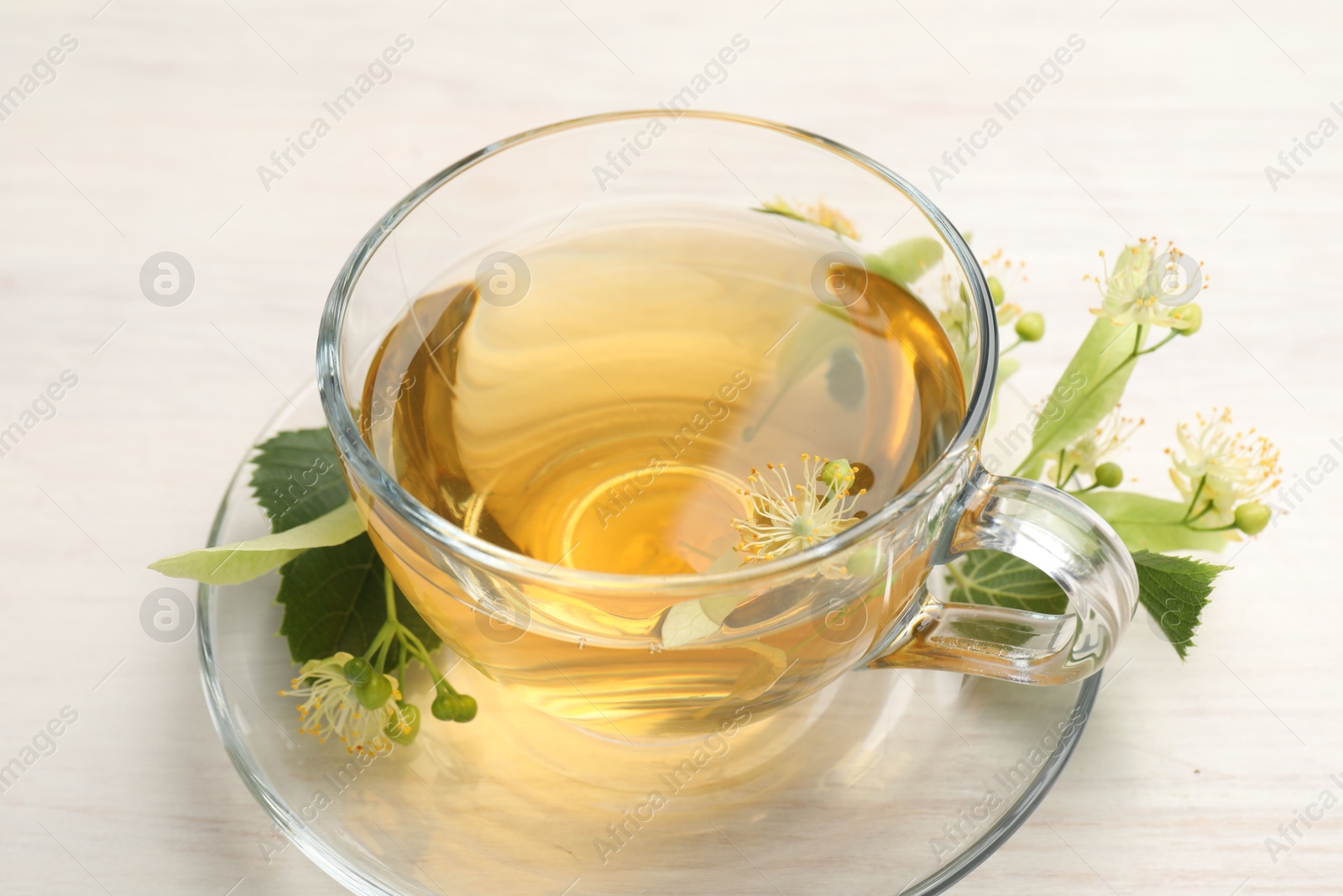 Fresh linden tea in cup and flowers on white wooden table, closeup Photo of Fresh linden tea in cup and flowers on white wooden table, closeup
