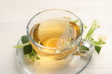 Photo of Fresh linden tea in cup and flowers on white wooden table, closeup