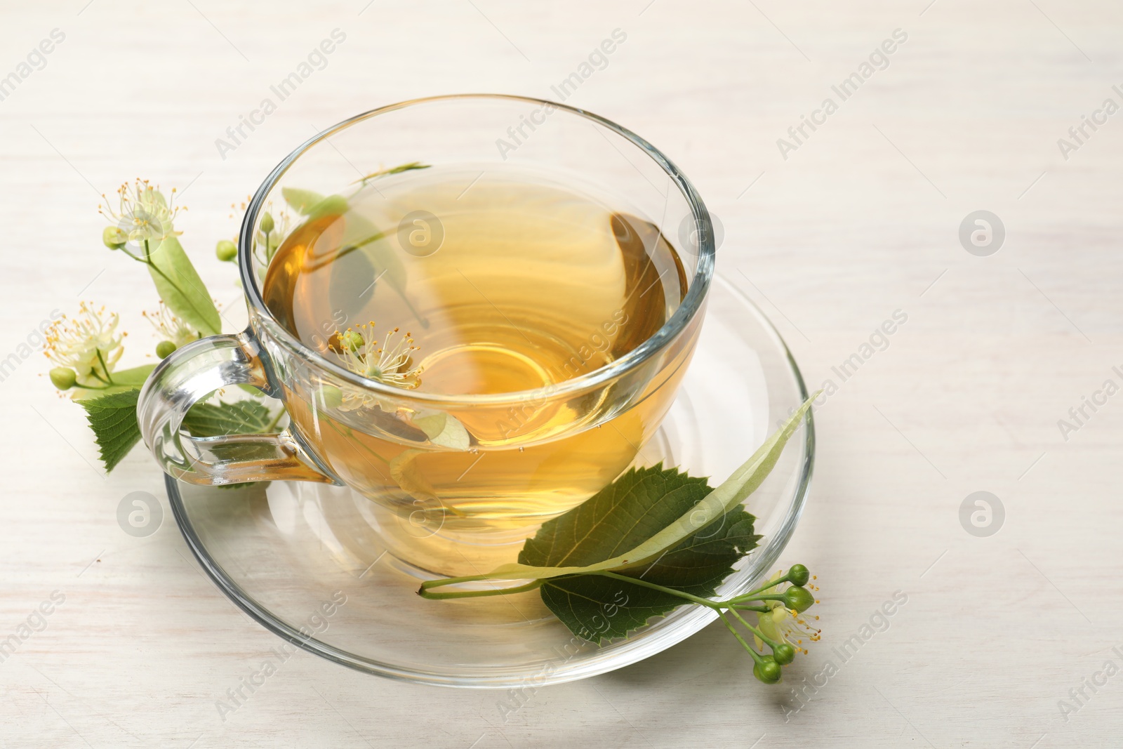 Fresh linden tea in cup and flowers on white wooden table, closeup Photo of Fresh linden tea in cup and flowers on white wooden table, closeup