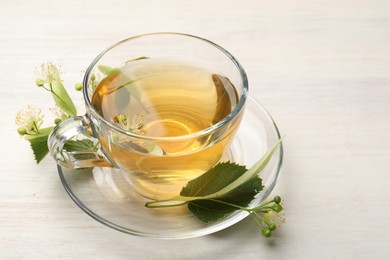 Photo of Fresh linden tea in cup and flowers on white wooden table, closeup