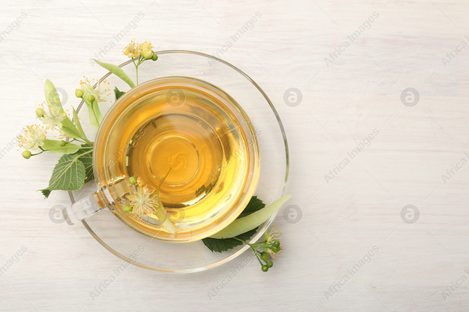 Fresh linden tea in cup and flowers on white wooden table, top view. Space for text Photo of Fresh linden tea in cup and flowers on white wooden table, top view. Space for text