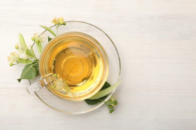 Photo of Fresh linden tea in cup and flowers on white wooden table, top view. Space for text