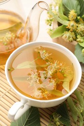 Photo of Fresh linden tea in cup, teapot and flowers on white table, closeup